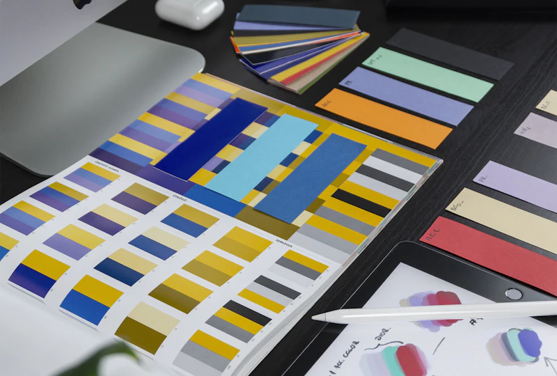 Graphic design workspace with colour swatch books and a tablet sketch
